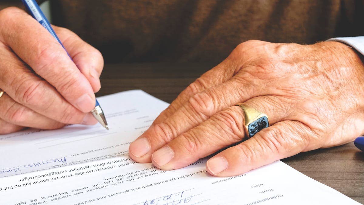 An older person's hand signing a written document