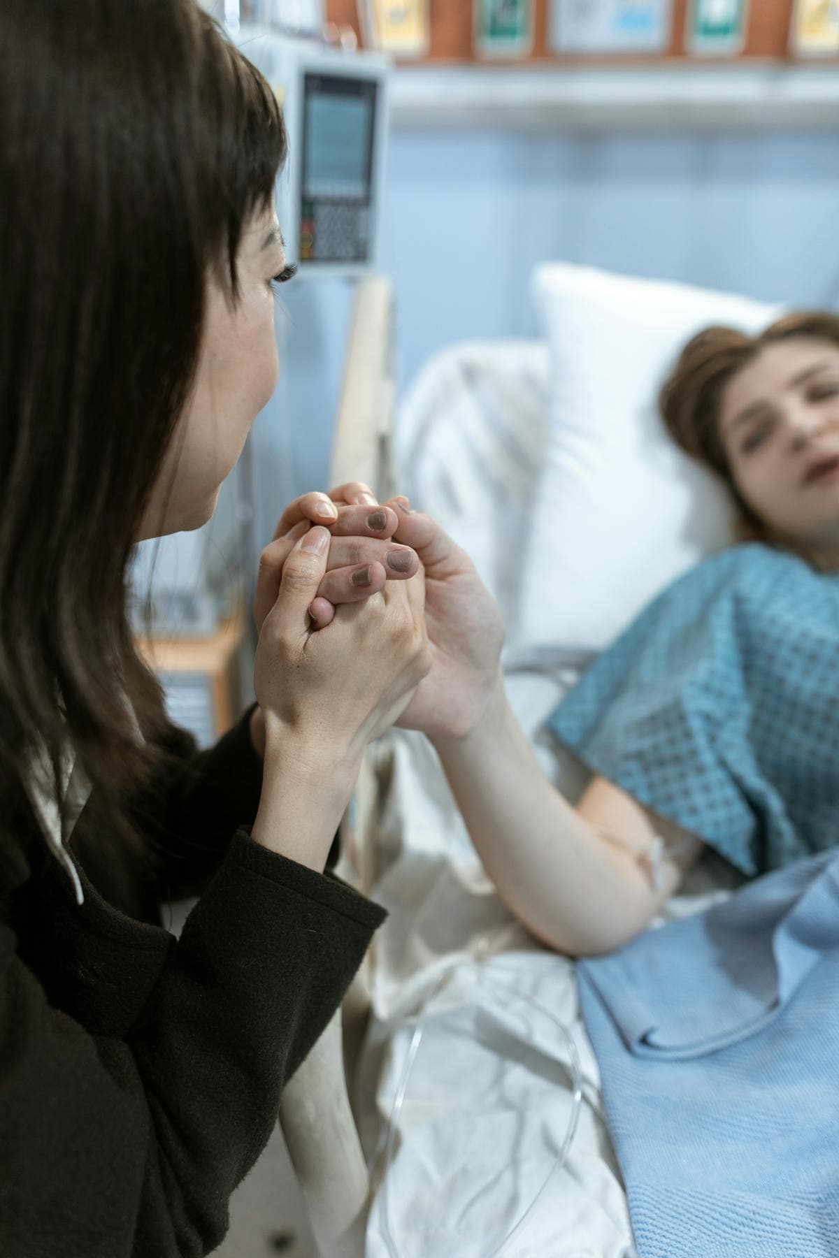 A carer holding the hand of a patient in a hospital bed